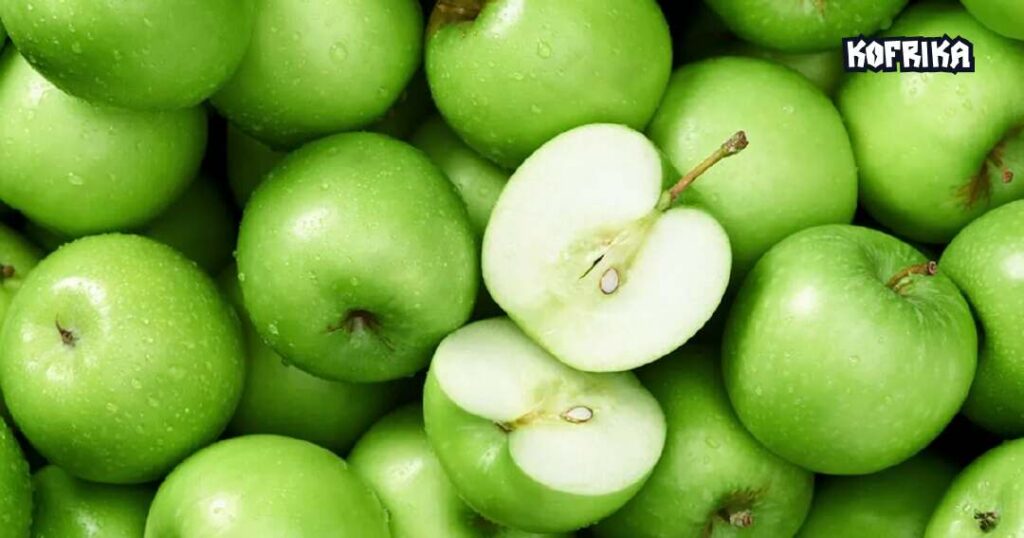 Many green apples are laid out to fill the entire image. One of the apples is sliced into half and in the centre of the image.